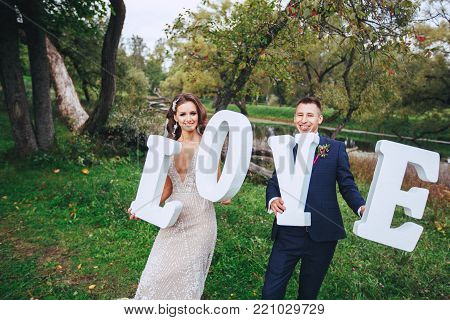 Happy wedding couple holding big white love letters . Bride and groom in park