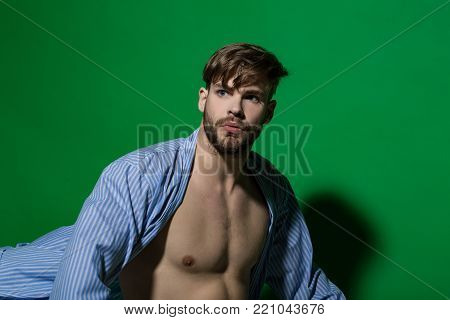 Spa, wellness, grooming. Man in blue dressing gown on green background. Macho with sexy torso in bathrobe. Home clothes, leisure wear. Fashion, style concept, copy space