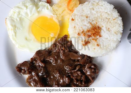 Tapsilog breakfast - typical morning food in Philippines. Garlic rice, fried egg and cured beef tapa.