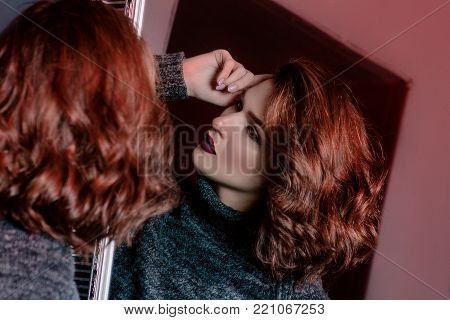 Portrait of crying near the mirror beautiful tender curly sad upset depressed lonely woman in gray sweater in dark room