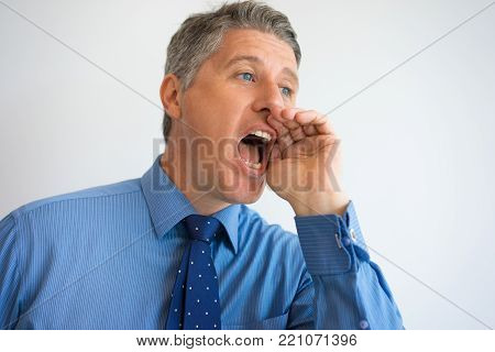 Portrait of excited middle aged Caucasian man in tie shouting loud with hand at mouth. Financial manager working. Top manager announcing important news. Announcement and important news concept