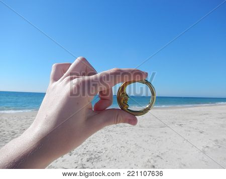 Golden Moon Clip Being Held, With A Big Blue Sky Backdrop And The Sandy Ocean Beach