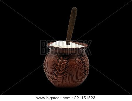 Clay sugar bowl full of sugar with a wooden spoon on a black background for cutout. Side view.