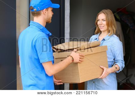 Smiling delivery man in blue uniform delivering parcel box to recipient - courier service concept. Smiling delivery man in blue uniform