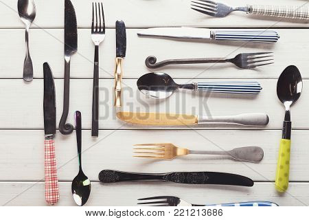 Top view on various forks, knives and spoons. Set of assorted cutlery with fancy handles, flat lay on white rustic wooden planks. Antique and modern kitchenwear background