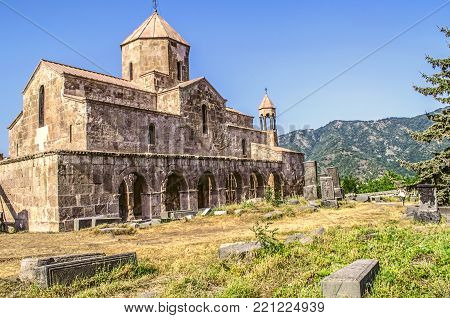 Odzun monastery on the south side at sunset, with views of the arched  gallery with the bell tower and basalt crosses in the background of forested mountains