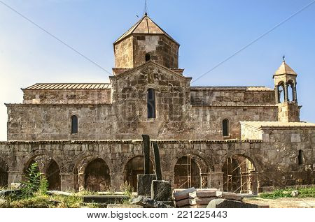 The southern side of Odzun monastery with arched gallery and a medieval cemetery at sunset