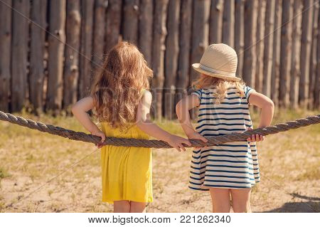 two children standing back to camera at the fence and talk