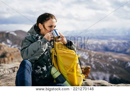 a tourist girl drinks hot tea on a background of snow-capped mountains