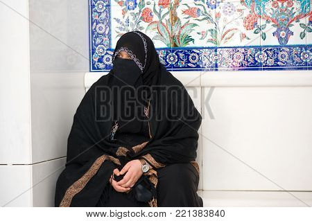 ABU DHABI, UNITED ARAB EMIRATES - DEC 28, 2017: Veiled muslima is sitting in the Sheikh Zayed Mosque in Abu Dhabi.