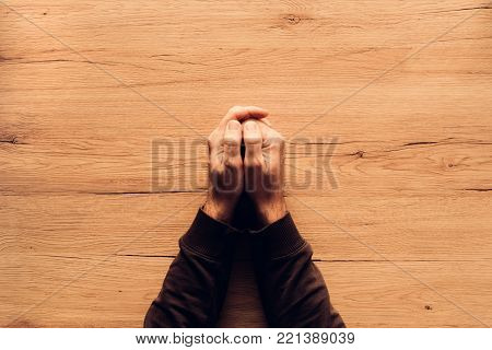Man praying, overhead view of male hands on wooden church prayer kneeler