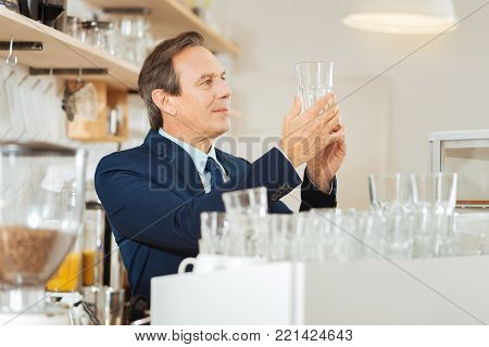 Perfect purity. Responsible concentrated occupied man standing on the kitchen holding and overlooking a glass.