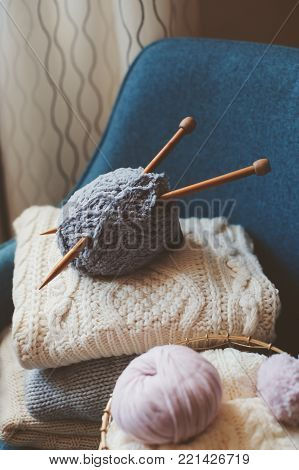 Grey and pink Yarn ball with knitting needles in metallic basket with knitted sweaters on background. Hobby, cozy homely weekend and hugge concept.
