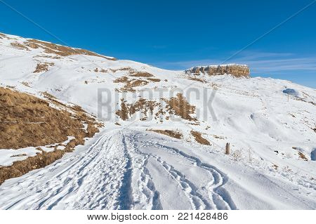 The landscape of snow-covered Caucasian rocks on the Gumbashi Pass. Snow-covered plateau passing into the table mountain with a snow trail in the foreground. Russia, Northern Caucasus