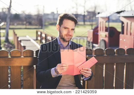 Handsome elegant man reading a love letter on Valentines Day at the park.