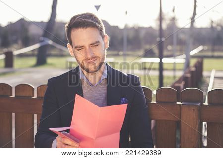 Handsome elegant man reading a love letter on Valentines Day at the park.