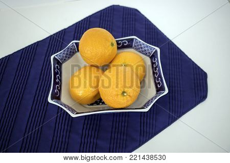 Several mandarin oranges in a blue and white oriental dish on blue placemat.