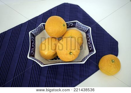 Several small mandarin oranges in oriental dish on bright blue place mat on white surface.