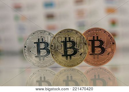 Close up of Bitcoins, gold bitcoin, silver bitcoin and bronze bitcoin with blurred background of world flags. reflection of the bitcoins visible