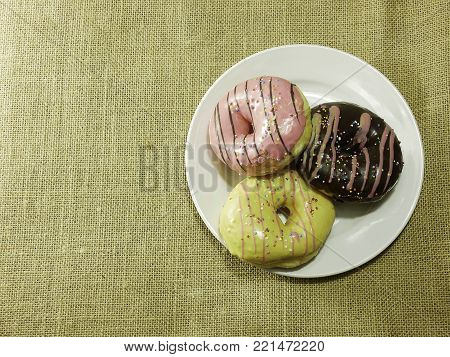 Flat lay Multicolored donuts on white dish brown color Hessian sackcloth woven background