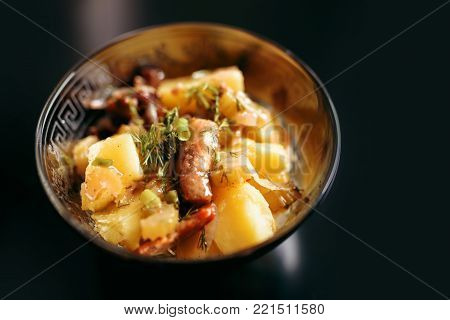 Potato salad with meat and greens in a plate on a black background
