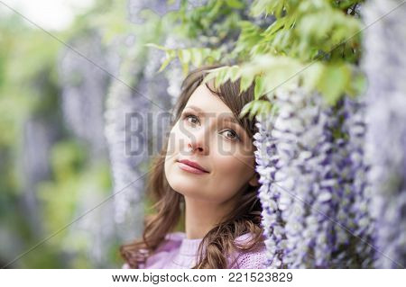 Portrait of a beautiful young brunette woman. A young woman is walking along the spring park. The girl is standing near the wisteria. Blooming park. Spring.