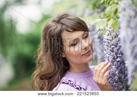 Portrait of a beautiful young brunette woman. A young woman is walking along the spring park. The girl is standing near the wisteria. Blooming park. Spring.