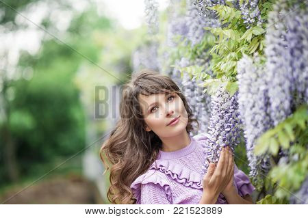 Portrait of a beautiful young brunette woman. A young woman is walking along the spring park. The girl is standing near the wisteria. Blooming park. Spring.