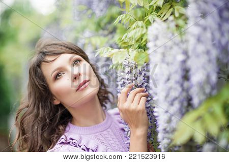 Portrait of a beautiful young brunette woman. A young woman is walking along the spring park. The girl is standing near the wisteria. Blooming park. Spring.
