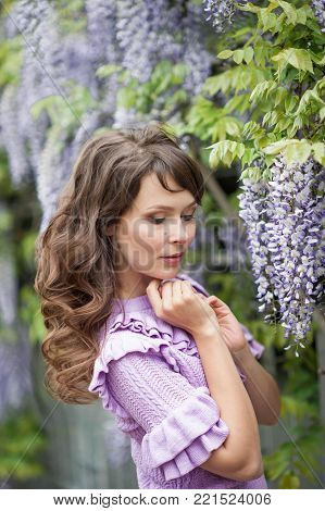 Portrait of a beautiful young brunette woman. A young woman is walking along the spring park. The girl is standing near the wisteria. Blooming park. Spring.