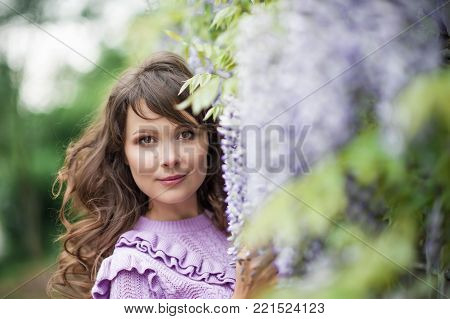 Portrait of a beautiful young brunette woman. A young woman is walking along the spring park. The girl is standing near the wisteria. Blooming park. Spring.