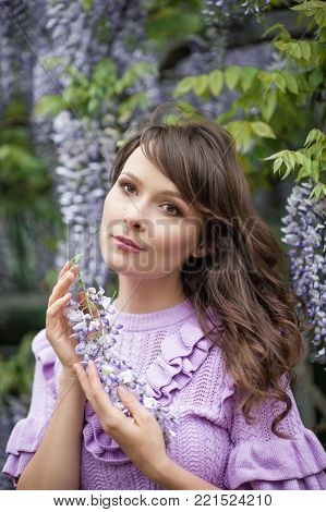 Portrait of a beautiful young brunette woman. A young woman is walking along the spring park. The girl is standing near the wisteria. Blooming park. Spring.