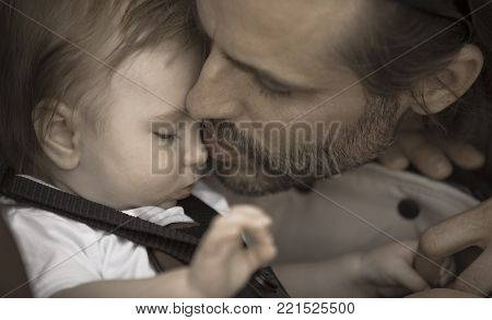 A father is kissing gently his young baby boy on the nose. Aged photo effect.