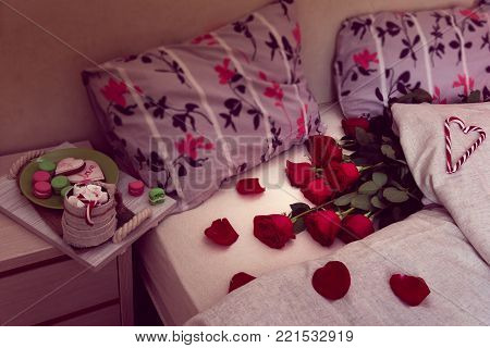 cozy still life of breakfast in bed for St. Valentine's Day. Coffee and cookie on a salver and red roses with his scattered petals on a bed with  two pillows