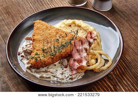 Chicken schnitzel with herb, mashed potatoes and mushrooms sauce on plate on wooden table background. Healthy food. Copy space. Still life. Served at restaurant, cafe, bar, pub