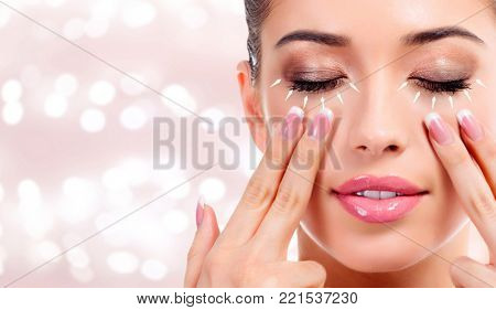 Pretty woman massaging her face, skin treatment antiaging concept. Abstract background with blurred lights