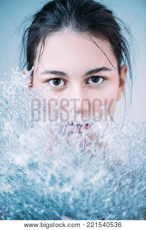 Beauty portrait. Sensual brunette girl with a white snowy plant. Winter look. Cosmetics, make-up. Perfumery.
