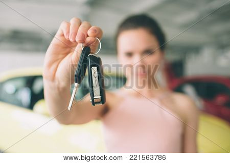 Beautiful young woman is holding a key in car dealership. Auto business, car sale, - happy female model in auto show or salon.
