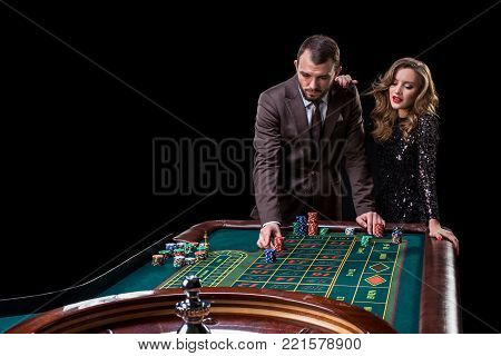 A man in a suit with a woman in a beautiful black dress playing roulette at the casino. Gambling. Casino. Roulette. Poker.