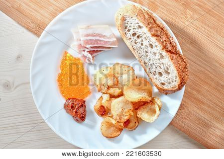Tasty harmful food. Greasy fried potatoes, bacon, red caviar, spicy sauce and white bread on a white plate. Snacking.