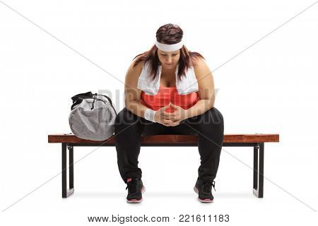 Sad overweight woman sitting on a wooden bench next to a sports bag isolated on white background