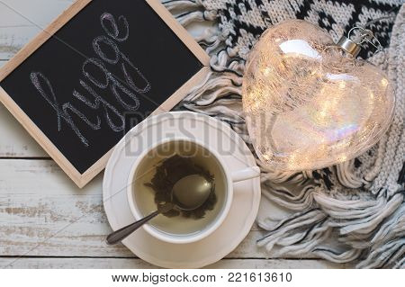 Cup of green tea, heart shaped lantern for house decoration, knitted blanket and blackboard with text "hygge". Hyggelig. Hygge concept. Top view