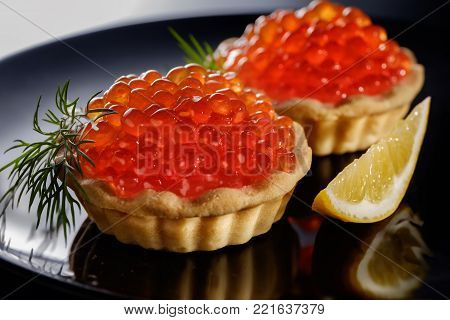 Tartlets with red caviar on black plate with piece of lemon