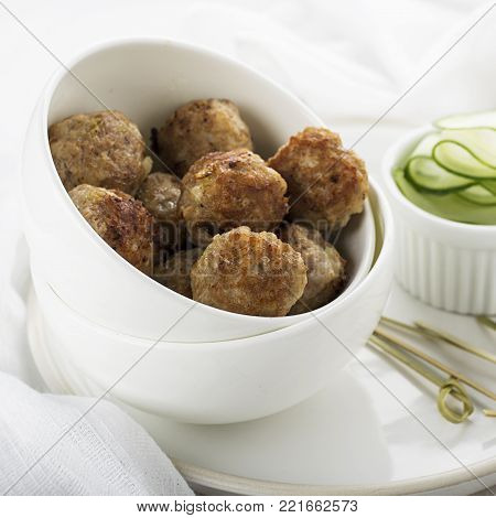 Meat home juicy meatballs in a white ceramic pial on a light background with cucumbers on a side dish. Selective focus