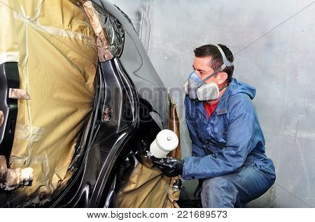 Worker painting a  black car in a paint boath.