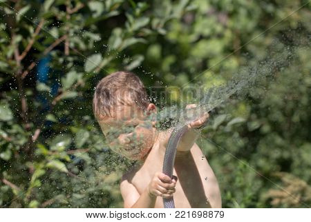 boy squirting water from a hose . In the park in nature
