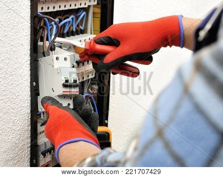 Young electrician technician introduces the electric cable into the clamp of the magnetothermic switch with an insulated clamp