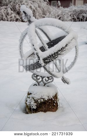 a frozen sundial standing in a garden full of snow in Sweden