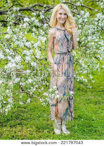 beautiful Russian girl blonde in a summer tight-fitting dress against the background of a blossoming apple tree