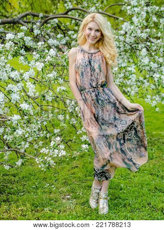 beautiful Russian girl blonde in a summer tight-fitting dress against the background of a blossoming apple tree